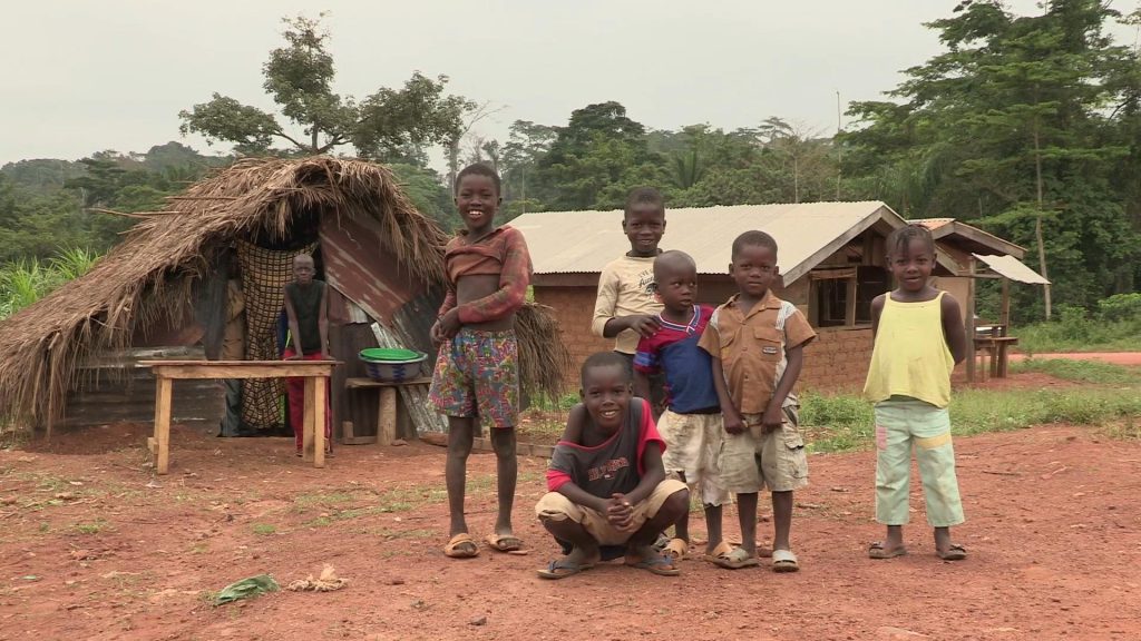 a camera shot with some african children in front of their house, which is made from corrugated metal with a straw roof