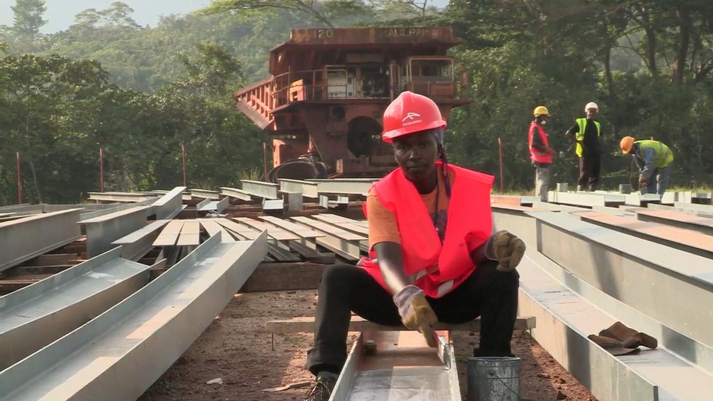 an african construction worker sitting on some steel beams with a big dump truck in the background